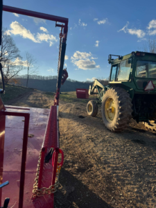 A Red-E-Bins dumpster on a rural property with a tractor and hydraulic trailer system, showcasing a scenic outdoor setting and professional dumpster rental services in Bristol, VA