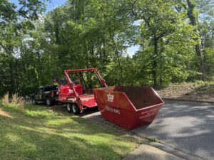Red-E-Bins truck delivering a bright red 15-yard dumpster to a residential driveway in Abingdon, VA, surrounded by green trees.
