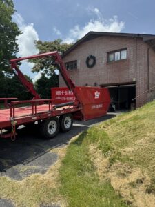 Red-E-Bins truck and trailer delivering a compact red dumpster to a residential property in Abingdon, VA.
